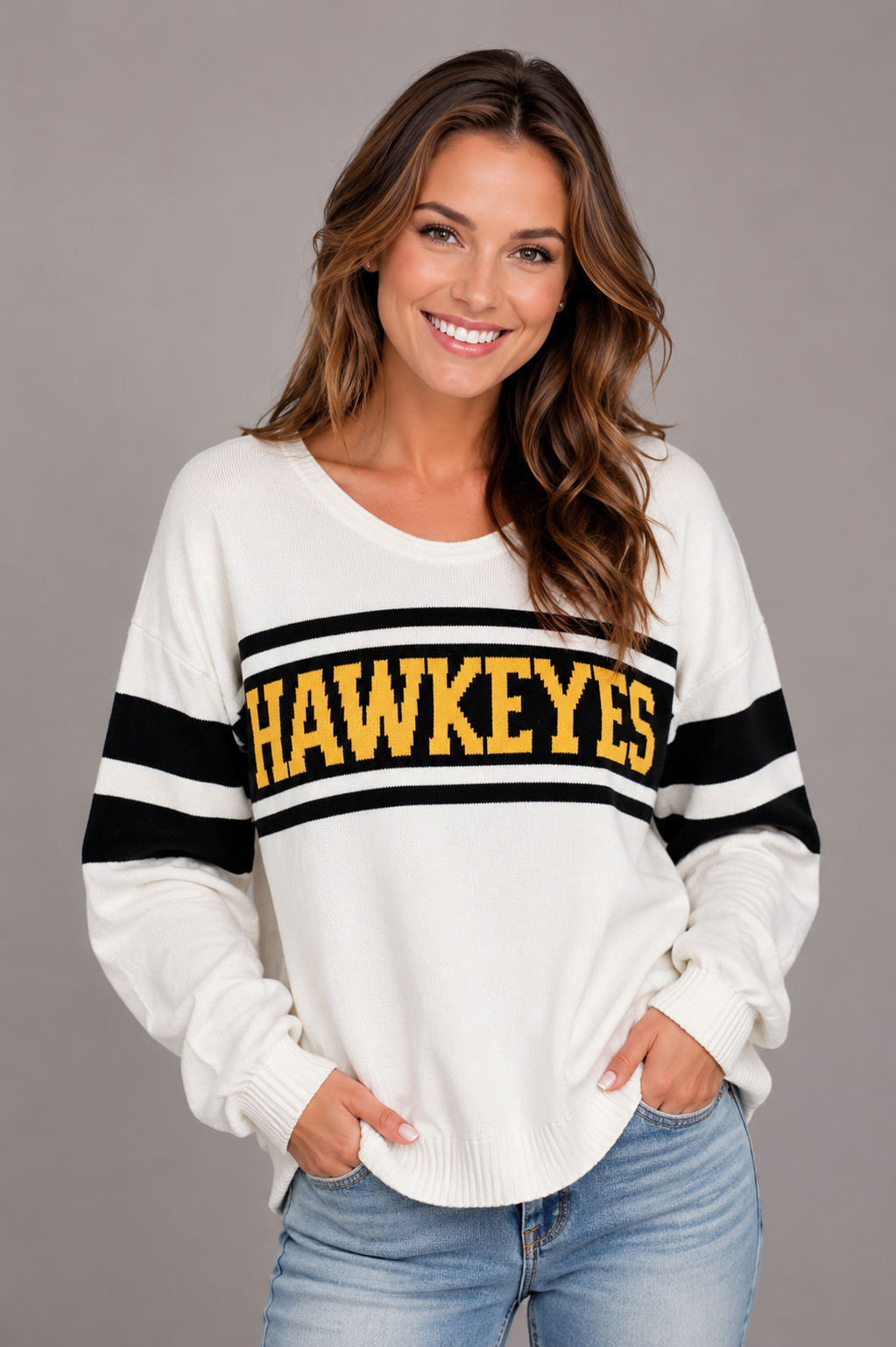 Model wearing the Iowa Hawkeyes Knit V-Neck Sweater in ivory, featuring black varsity sleeve stripes and bold gold HAWKEYES lettering across the chest.