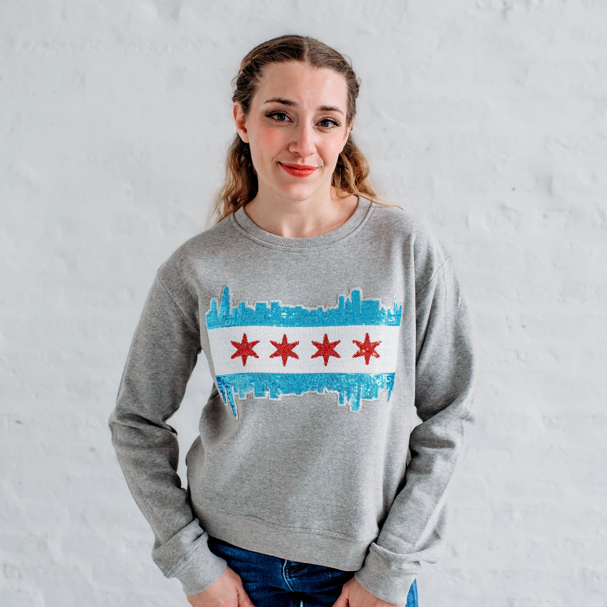 Person wearing a gray sweatshirt with a Chicago skyline design against a white brick wall.