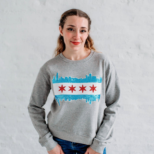 Person wearing a gray sweatshirt with a Chicago skyline design against a white brick wall.