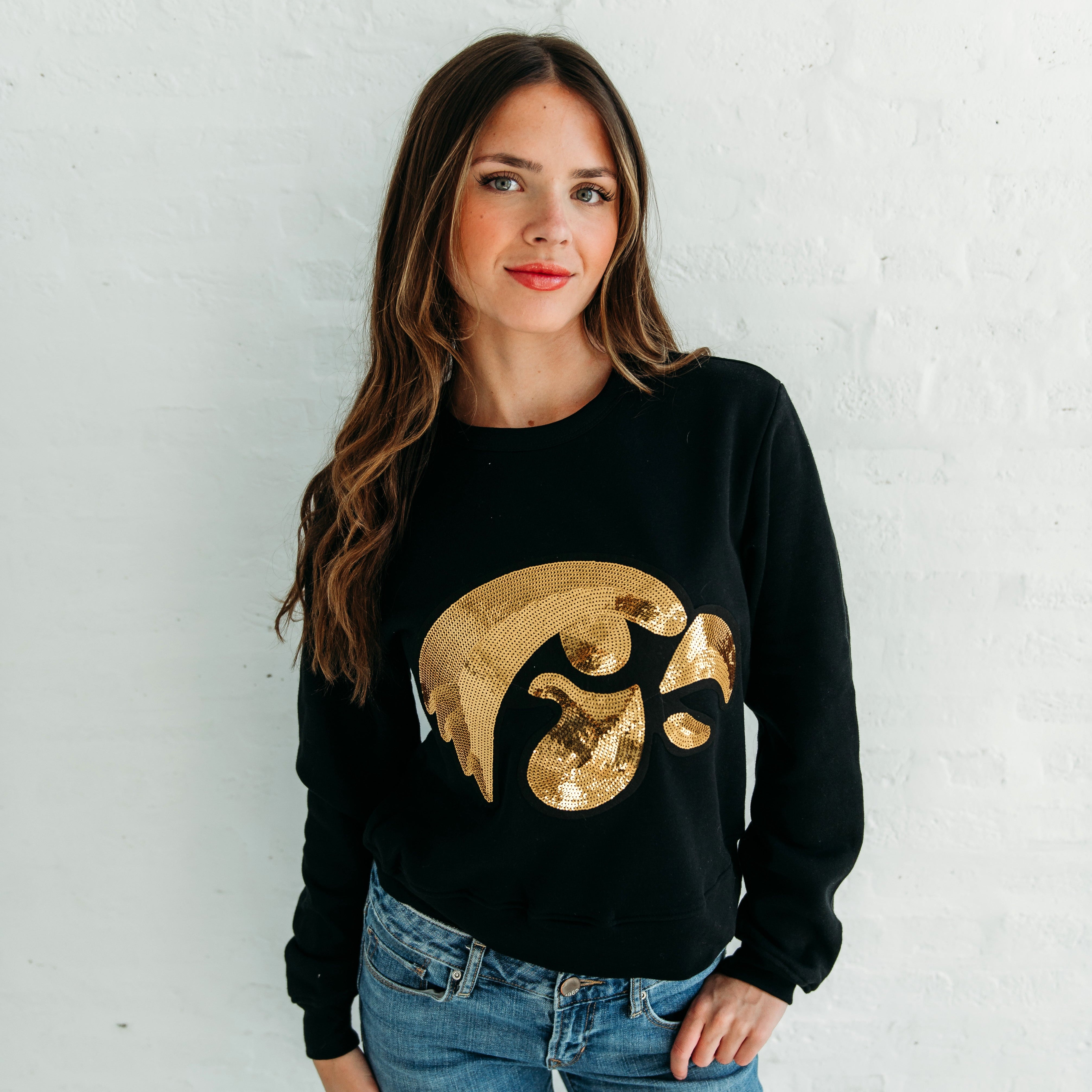 Close-up of a model wearing the Iowa Tigerhawk Sequin Women's Crewneck in black, featuring an oversized gold sequin Tigerhawk logo across the front.