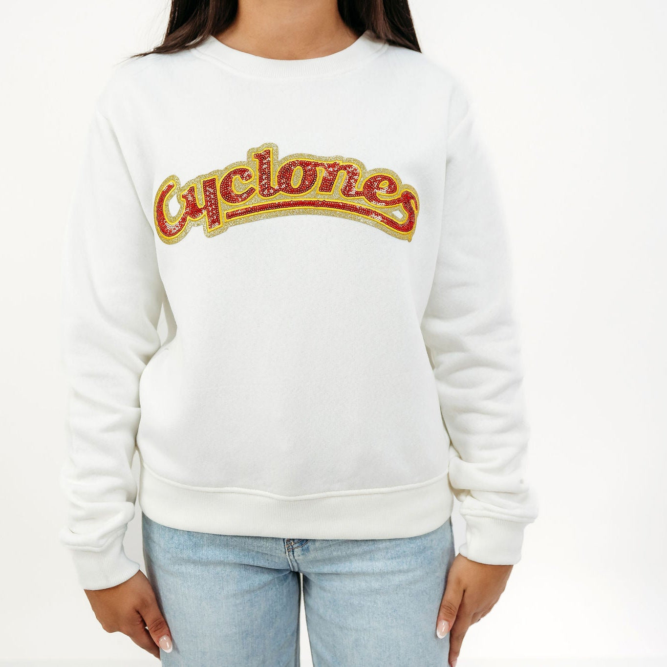 A person wearing a white crewneck sweatshirt with a retro arched 'Cyclones' logo across the chest in red and gold, paired with light blue jeans, against a plain white background.