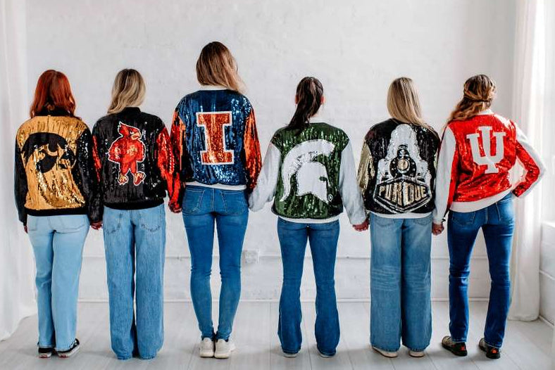 Five women wearing letterman jackets with various designs and letters on a white background